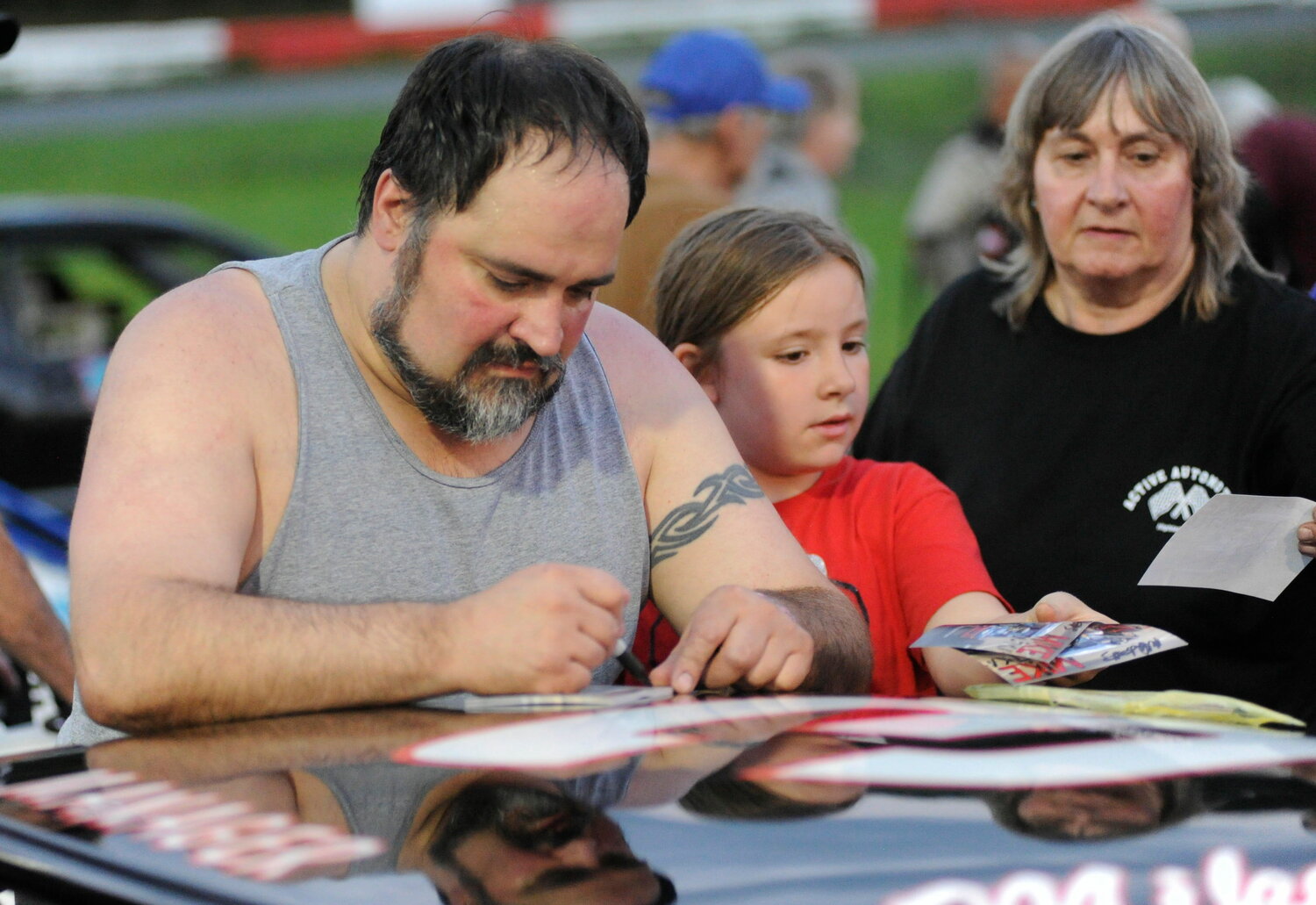 Mike Dutka, a noted NASCAR asphalt modified driver, signs a photo for a young fan of auto sports.